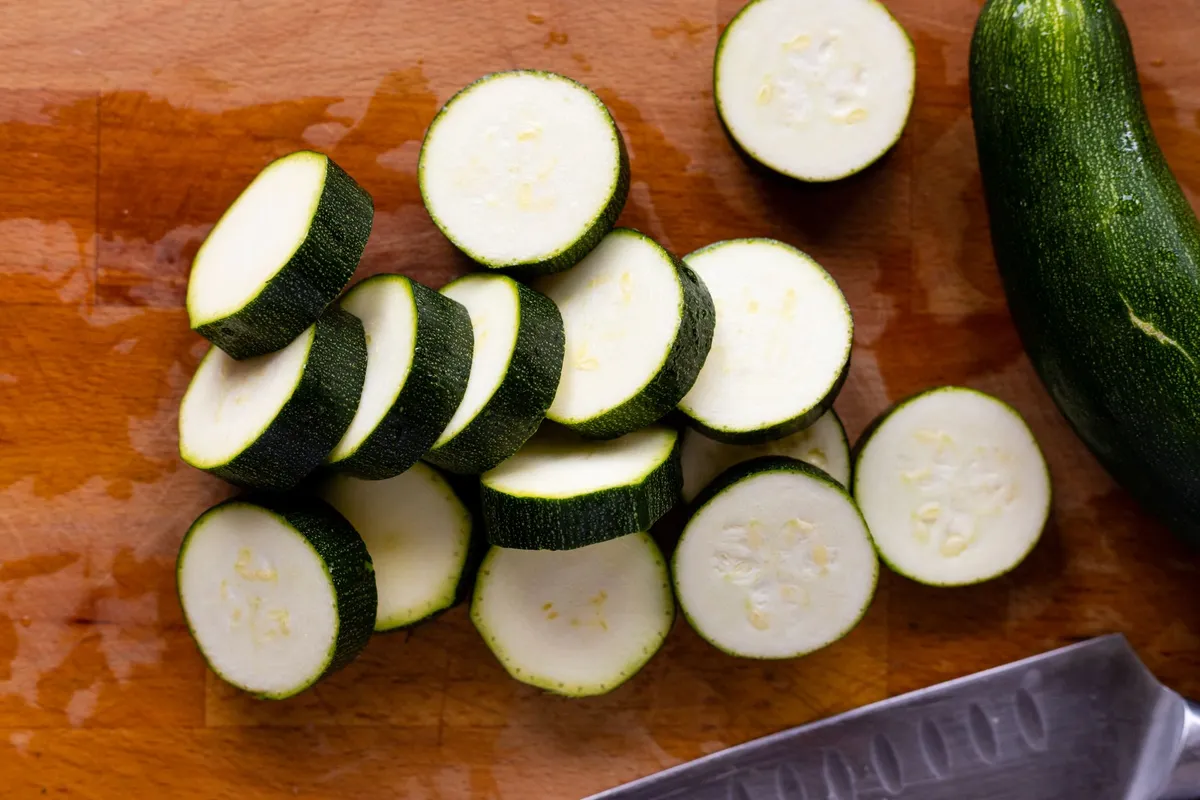Frisch geschnittene Zucchinischeiben auf einem Holzbrett, bereit zum Einfrieren oder Einkochen.